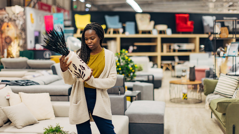 A woman holds an expensive vase in a store and looks concerned about the price