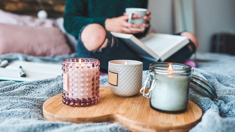 a person holding a cup with three candles in glass jars on a tray