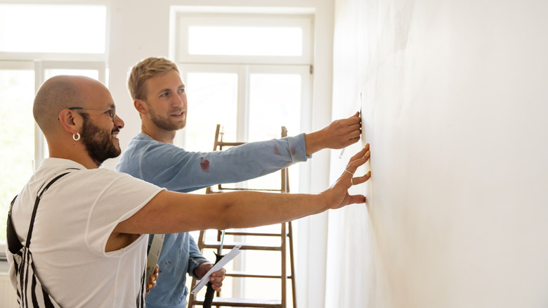 Two men with their hands on the wall discussing painting ideas
