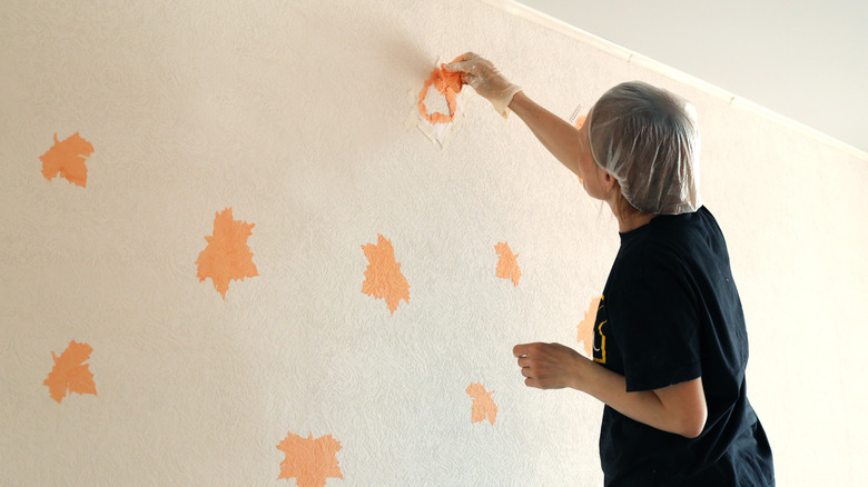 A person wearing a hairnet adding orange maple leaf stencils to a cream wall