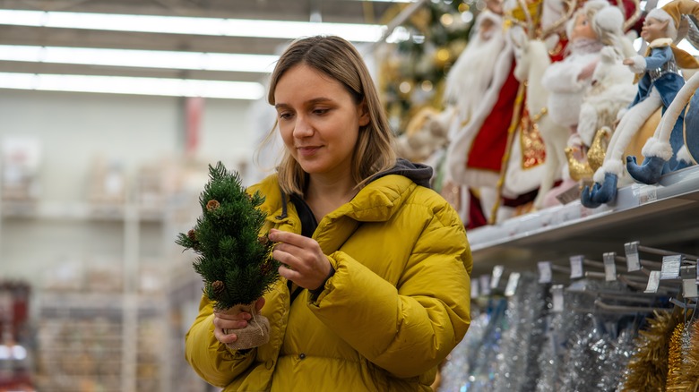 A woman holds a mini Christmas tree in her hands while shopping at a dollar store.