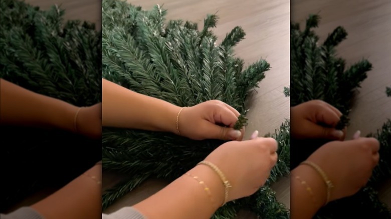 A TikToker ties two Dollar Tree Christmas trees together using wired faux pine branches.