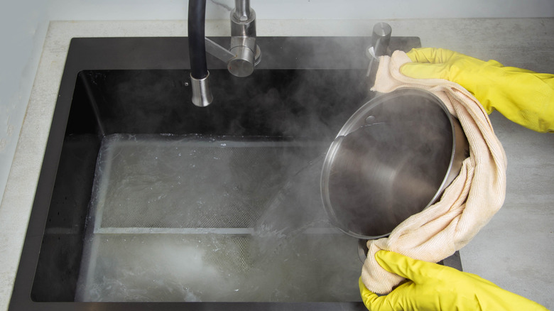 Gloved hands pouring boiling water into sink
