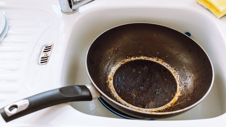 Greasy frying pan in white kitchen sink