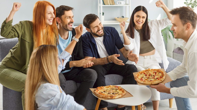 Woman sits on arm of crowded couch