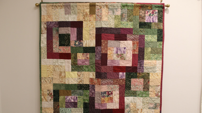 A quilt hangs on a wall from a curtain railing in a home.