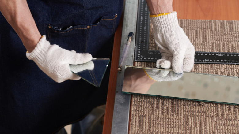 A gloved person snaps a piece of mirror along a cut line