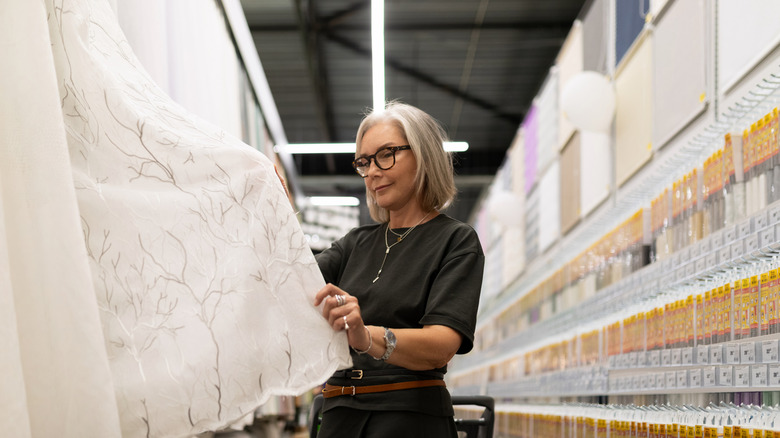Woman looking at lace curtain sample in store.
