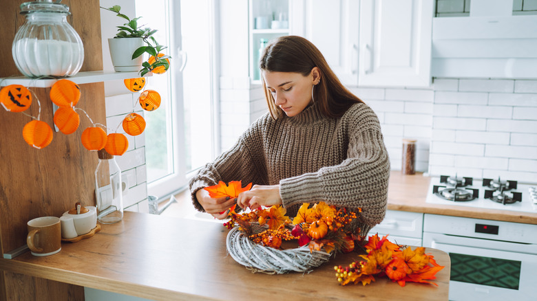 A woman stands at her kitchen counter making a fall decor wreath.