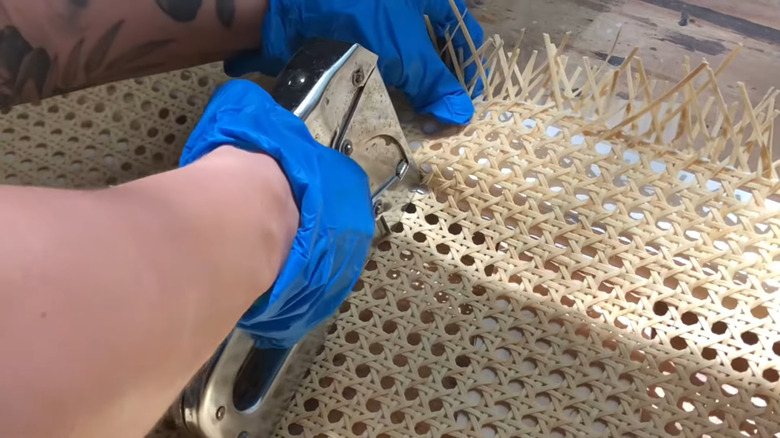 Person stapling cane webbing to door.
