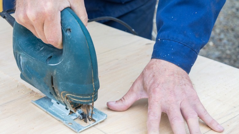 Person cutting out shape from plywood piece with jigsaw.