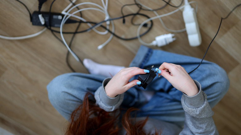 A woman wrapping up tangled power cords while sitting on the floor