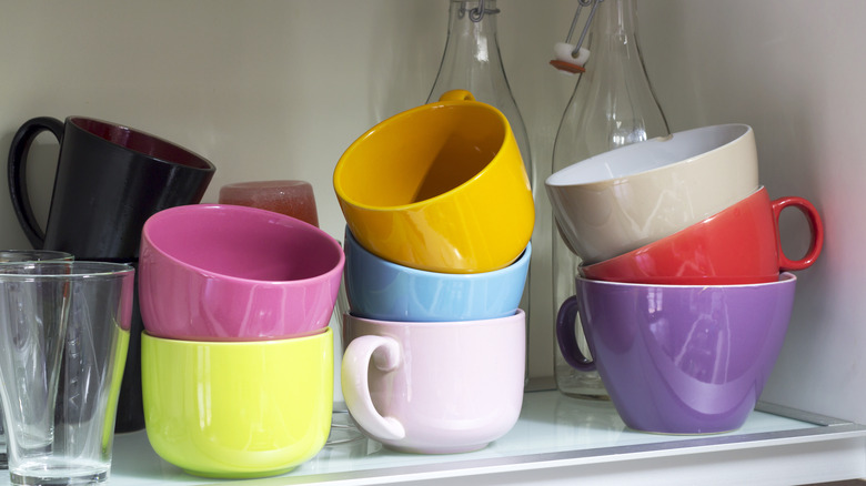 Colorful coffee mugs are stacked in a white kitchen cabinet.
