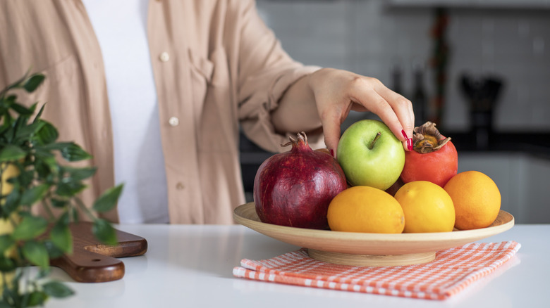 A woman reaching into a fruit basket.