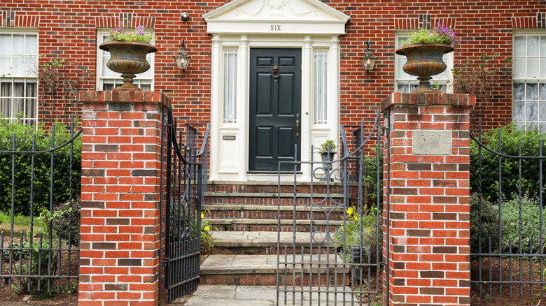 A wrought iron fence and gate is in front of a handsome Colonial brick home