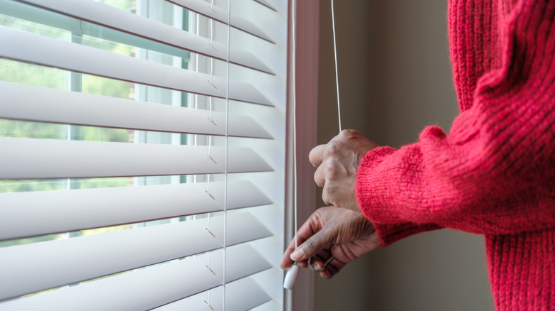 A woman in a red sweater opening her blinds