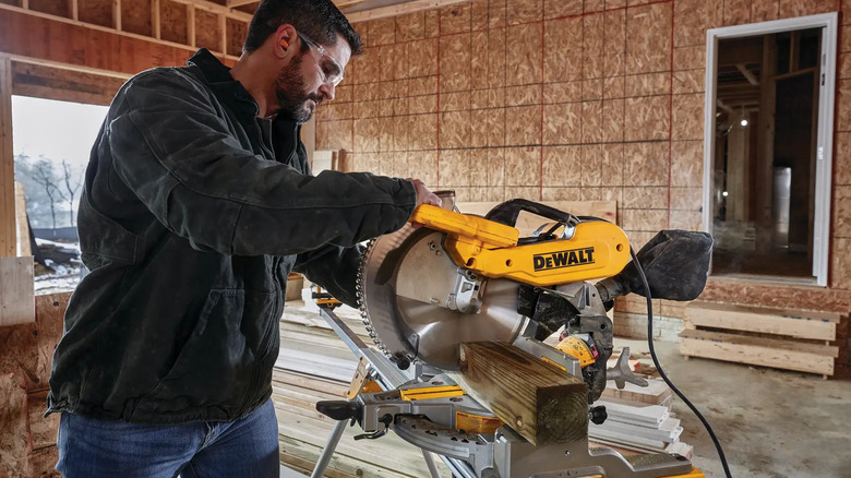 A man using the DeWalt Dual Bevel Compound Corded Miter Saw on a home project as he cuts through a 4 by 4