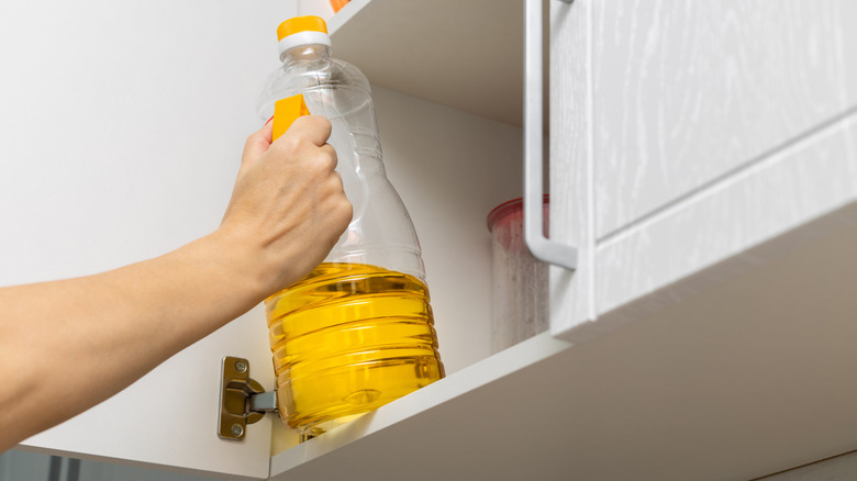 A person reaches up to pull a bottle of cooking oil from a kitchen cabinet.