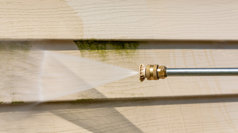 Close-up of power washer removing green grime on vinyl siding