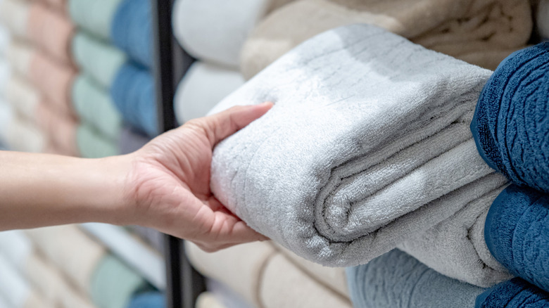 A person grabbing a nicely folded towel off of a shelf in a store