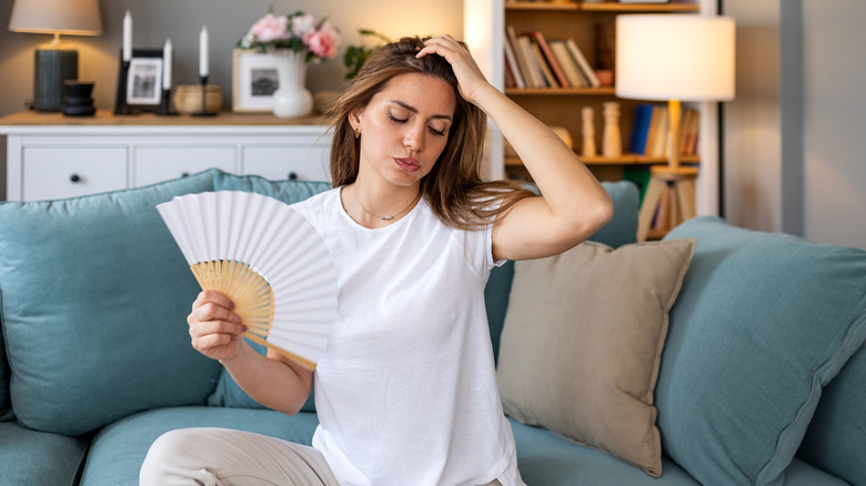 A woman sitting on a couch and holding a paper fan