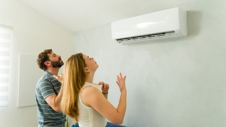 A couple standing in front of a mini split AC to cool themselves