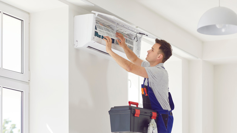 A man in blue overalls and tools is taking out the dirty filter from a mini split AC