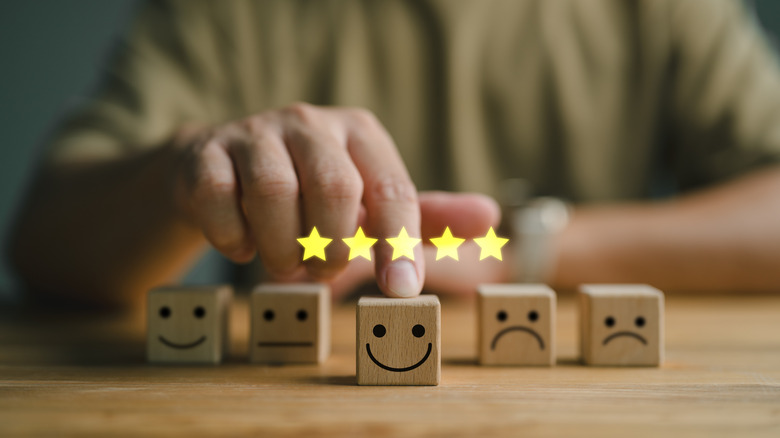 Five blocks with happy and sad faces in a row and a hand pushing the smiling block forward with a five star icon above it