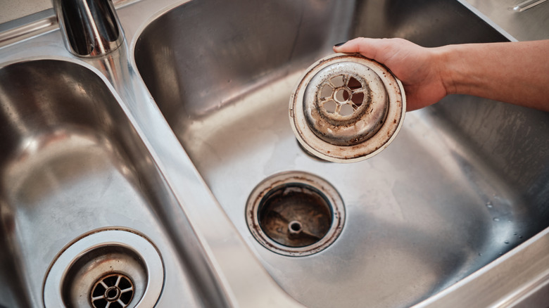 Stainless steel kitchen sink with hand holding a dirty drain stopper