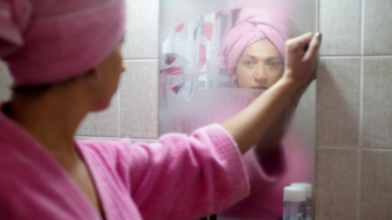 Woman wiping steam off mirror