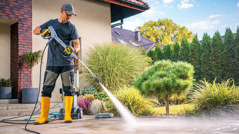 A man using a pressure washer to clean a patio