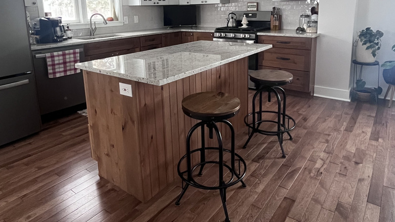 A boring, outdated wood-panel island in a kitchen with wooden floors and cabinets.