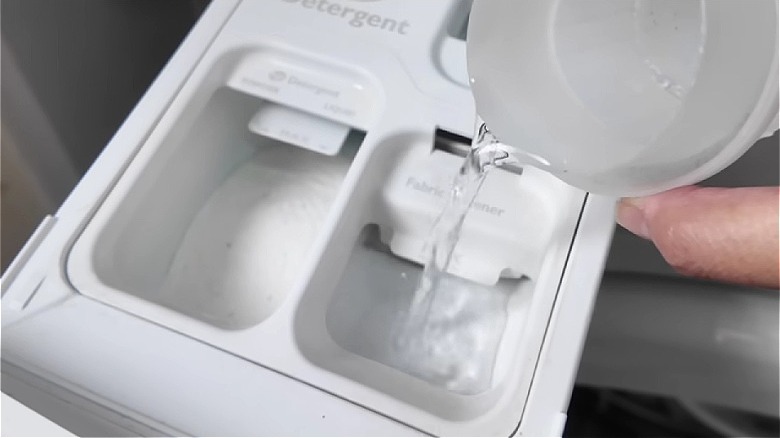 Hand pouring vinegar into washing machine compartment to brighten white clothing.
