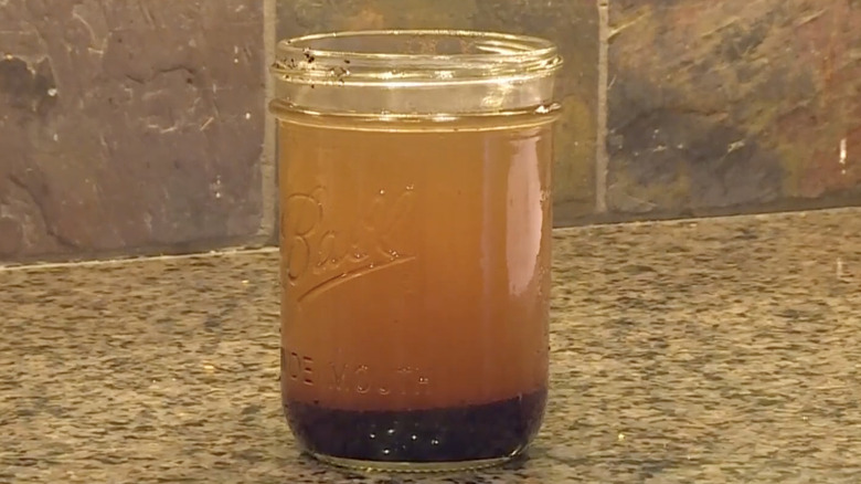 A jar of coffee grounds and water sits on a granite countertop in the kitchen.