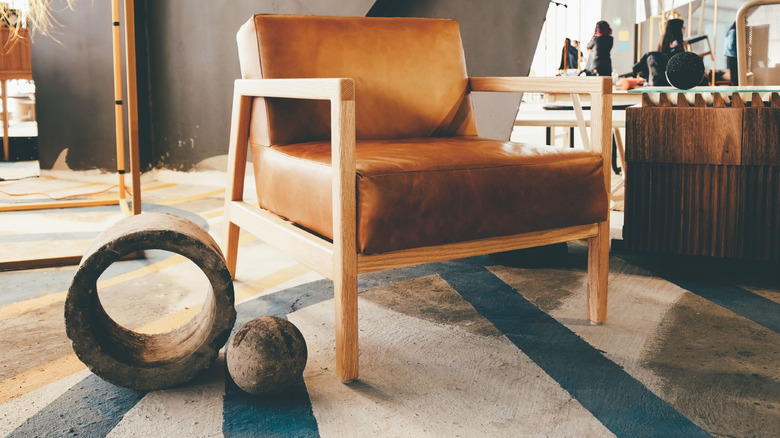 A close-up of a leather armchair on a concrete floor, beside two decorative stone objects