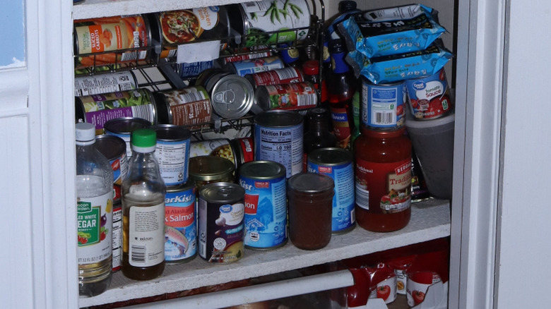 An interior view of a kitchen cabinet cluttered with canned goods