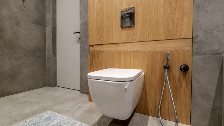A minimalist toilet with a bidet on the side hanging on a wooden wall in a modern bathroom