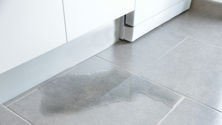 Water spilled on the gray tiled floor in a kitchen.