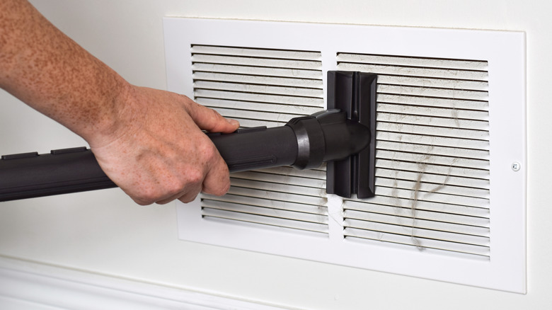 A person uses a vacuum and attachment to clean an air vent
