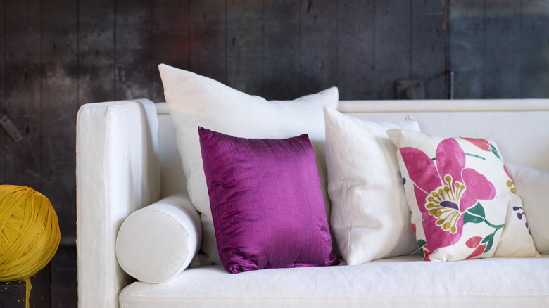 White couch with pillows of varying sizes, including a pink shiny fabric pillow and a floral pillow