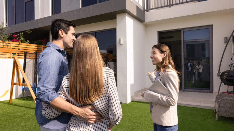 A young couple talking to a real estate agent in front of a home that's for sale
