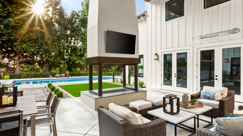 Beautiful backyard patio with a fireplace, TV, seating, and a pool in the background.