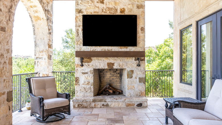 Stone balcony with a TV above an outdoor fireplace.