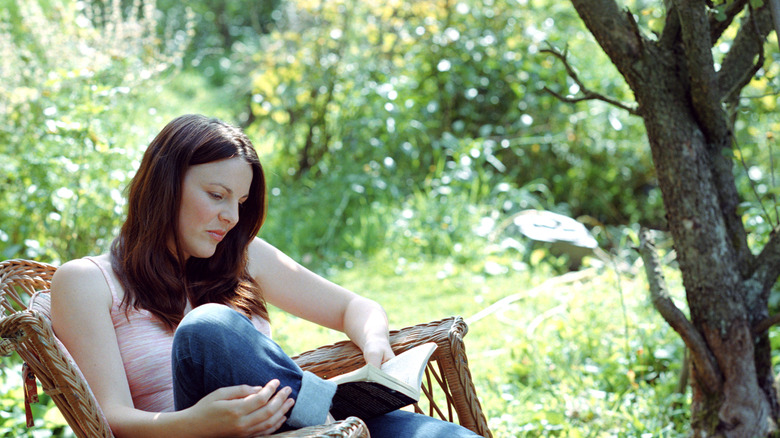 A woman relaxes with a book near a shade tree