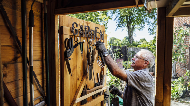 Man hanging up garden equipment neatly in shed