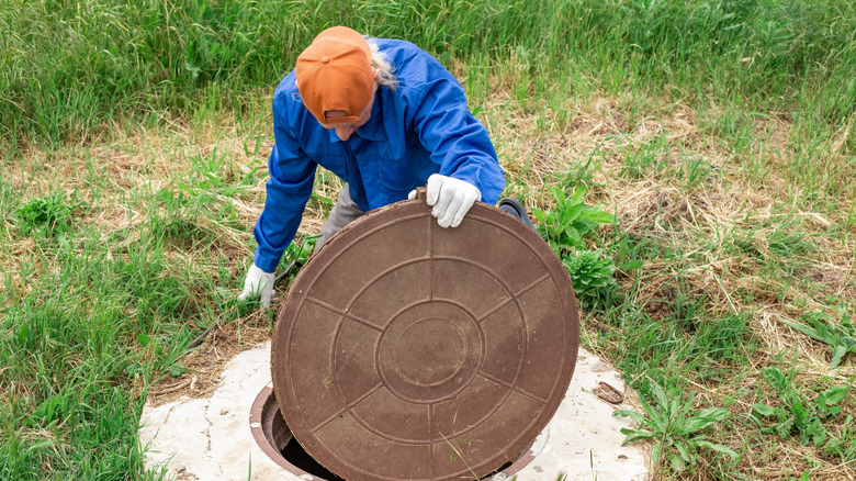 A person opening a septic tank lid in an overgrown grassy field