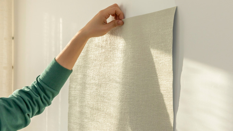 Person holds peel-and-stick wallpaper against the wall, choosing the right one for their DIY accent wall.
