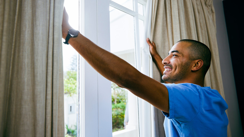 man opening window curtains