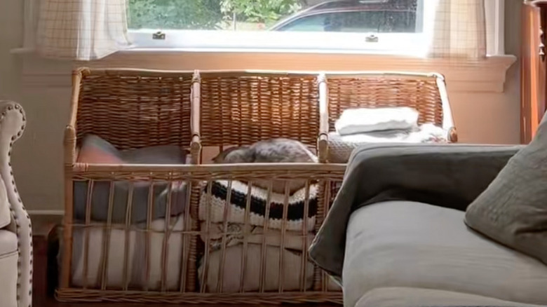 A brown vintage wicker baguette basket filled with spare blankets in a living room.