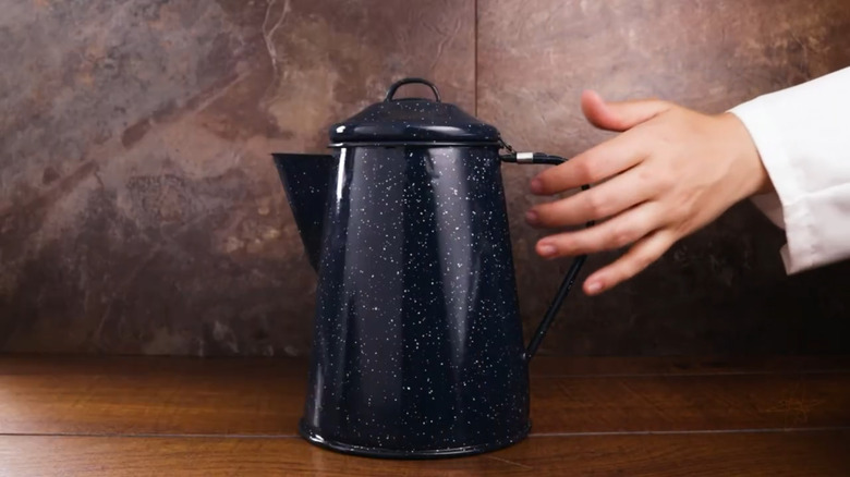 A hand reaches for a blue granite coffee pot.